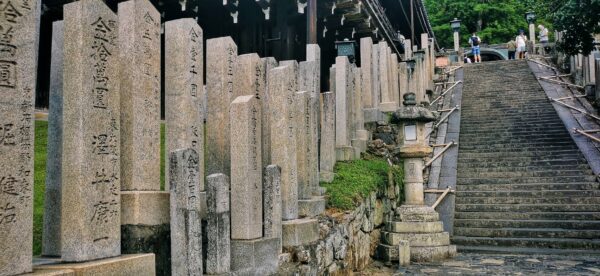 Des stèles avec des écritures en kanji sur la gauche d'un escalier menant vers un temple.